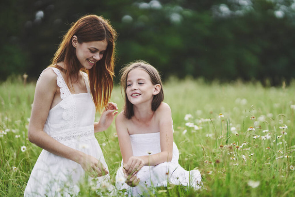 Young mother and her daughter having fun on camomile field - Фото, изображение