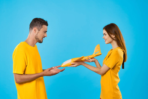 Young beautiful couple playing with yellow toy plane on blue background  - Фото, изображение