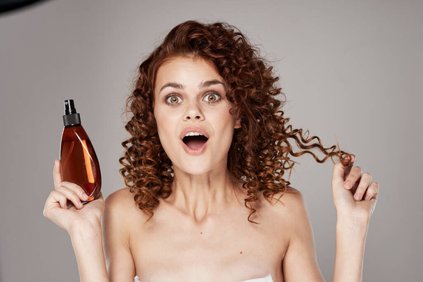Joven hermosa mujer con cabello rizado sosteniendo spray para el cabello. Captura de estudio
 - Foto, imagen