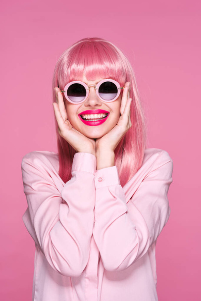 młoda piękna kobieta w różowej peruce i okularach przeciwsłonecznych pozowanie w studio  - Zdjęcie, obraz