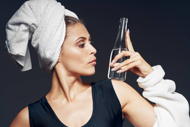 Studio shot. Young fit woman in bathrobe with bottle of water on dark background   - Foto, afbeelding