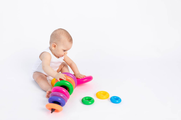 Cute maluch chłopiec 8 miesięcy w białym body gra z rozwojem zabawki siedzi na białym tle, miejsce na tekst - Zdjęcie, obraz