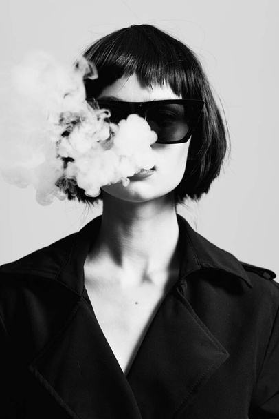 Giovane bella donna in occhiali da sole fumare in studio. Fotografia di moda  - Foto, immagini