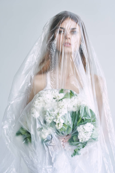 Young woman under plastic sheeting holding flowers. Ecology concept - Fotografie, Obrázek