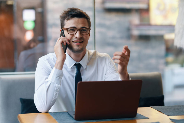 Fiatal üzletember laptoppal beszél okostelefonon az irodában  - Fotó, kép