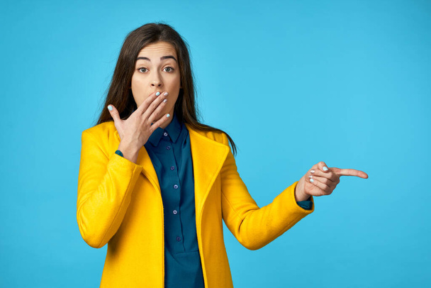 Young woman in yellow jacket  pointing  on  blue background. - Photo, image