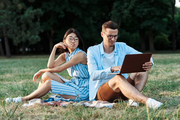 mladí studenti s notebookem sedí na trávníku  - Fotografie, Obrázek