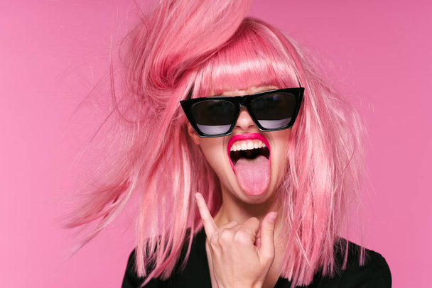 fiatal nő rózsaszín paróka mutatja nyelv rózsaszín háttér - Fotó, kép