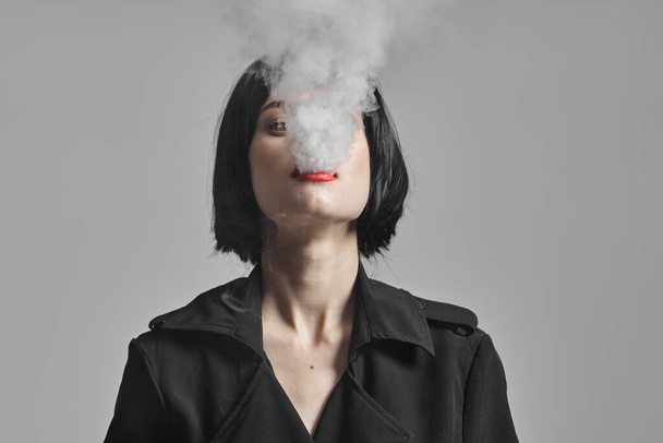 Μια νεαρή όμορφη γυναίκα καπνίζει στο στούντιο. Φωτογραφία μόδας  - Φωτογραφία, εικόνα