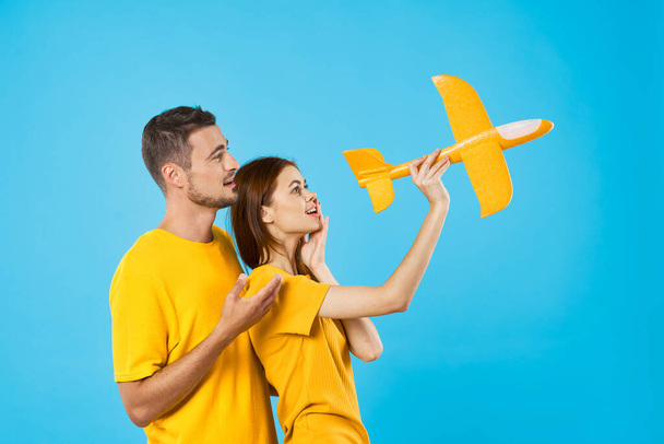 Joven pareja hermosa jugando con el avión de juguete amarillo en fondo azul  - Foto, Imagen
