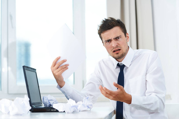 Joven hombre de negocios enojado en la oficina con documnets y portátil - Foto, Imagen
