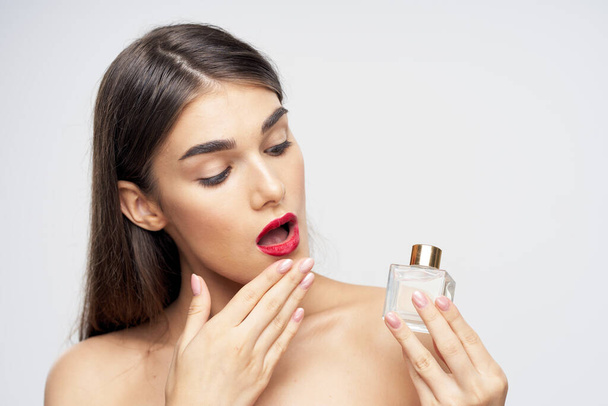 Young beautiful woman holding perfume bottle in studio - Foto, imagen