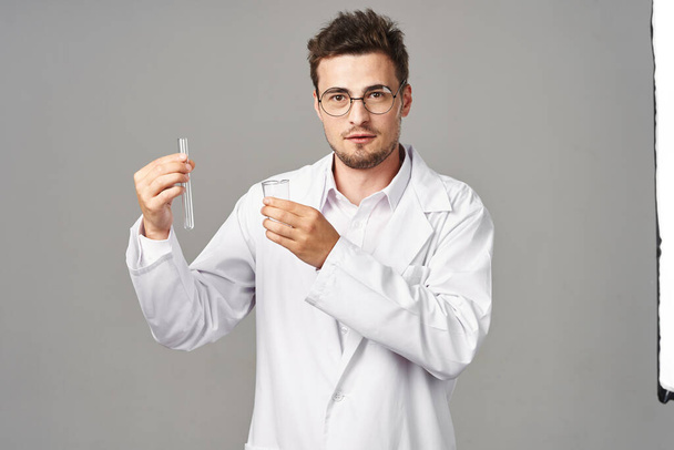 Genç yakışıklı doktor gri arka planda test tüpleri tutuyor. - Fotoğraf, Görsel