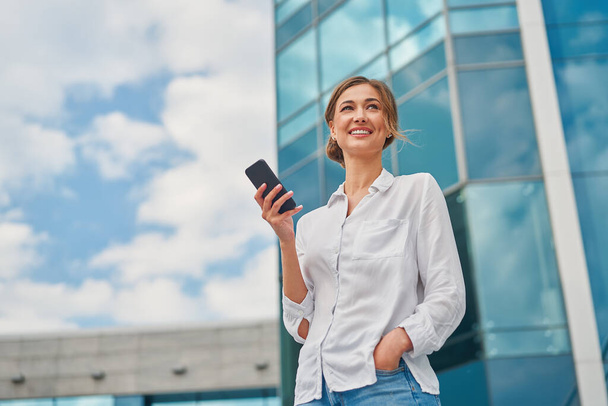 Businesswoman successful woman business person standing outdoor corporate building exterior cell phone Pensive elegance cute caucasian professional business woman middle age dreaming with mobile phone - Photo, image
