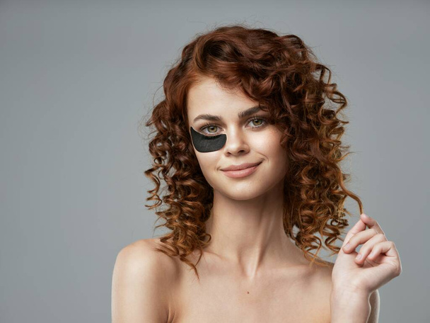 junge schöne Frau mit lockigem Haar mit Augenklappe im Studio             - Foto, Bild