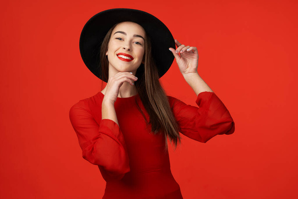 Studio shot. Young beautiful woman in  hat posing isolated on red background - Photo, Image