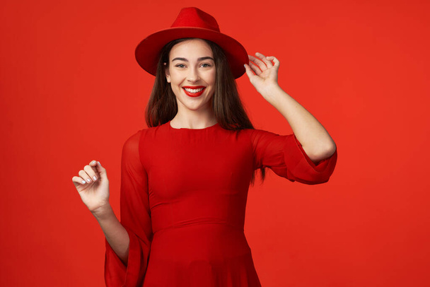Prise de vue. Jeune belle femme en chapeau rouge isolé sur fond rouge - Photo, image