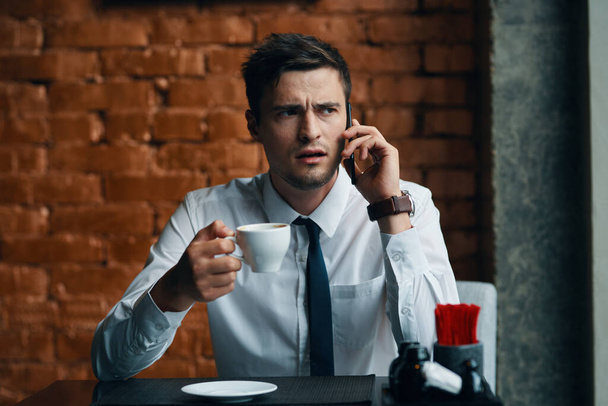 молодой привлекательный бизнесмен в кафе разговаривает по смартфону - Фото, изображение