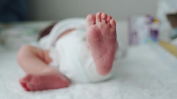 Małe nóżki noworodka. Dziecko porusza nogą. Rozproszyć. Nowe życie. Dziecko w pieluszce na pieluszce na stole w pomieszczeniu - Materiał filmowy, wideo