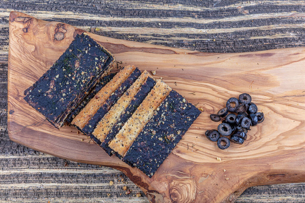 Crispy cookies with olives, vegetable crackers on olive wood cutting board. Mediterranean food concept. - Photo, image