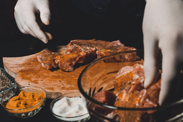 Marinoin raakaa sianlihaa kebabien ja kinkun keittämiseen. Ravintolan käsineiden keittiömestari käsittelee lihaa basilikan ja curryn mausteilla 2021. - Valokuva, kuva