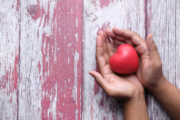 человек, держащий красное сердце в руках на деревянном столе
 . - Фото, изображение