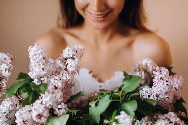 Beautiful girl with lilac flowers in her hands. A girl with lilac flowers in the spring at home. A girl with long hair and lilac in her hands. - Foto, immagini