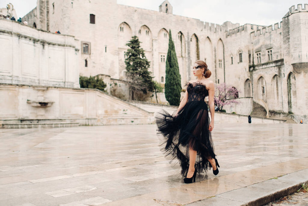 A stylish bride in a black wedding dress poses in the ancient French city of Avignon. Model in a beautiful black dress. Photo shoot in Provence - Fotó, kép