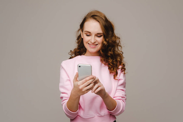 A happy young girl holding a phone looks into it and smiles. - Foto, Imagen