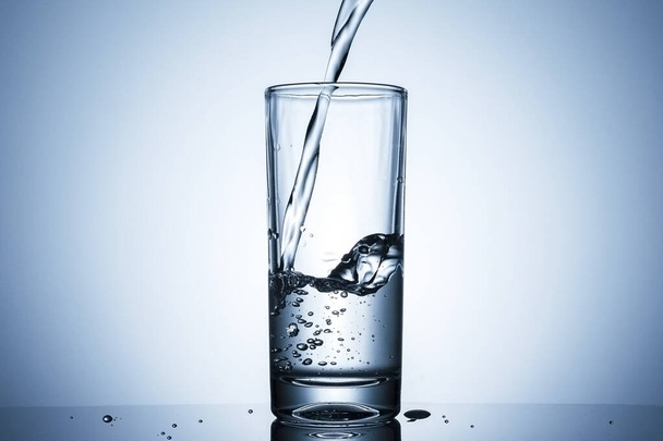 Giet sprankelend water in een glas van dichtbij op de rand van de met bruisende belletjes - Foto, afbeelding