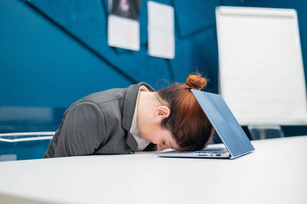 Exhausted Frustrated business woman put her head down on a notebook sitting at a desk. A female employee worked overtime and fell asleep at a computer in the office. Hard worker. - Foto, Imagen
