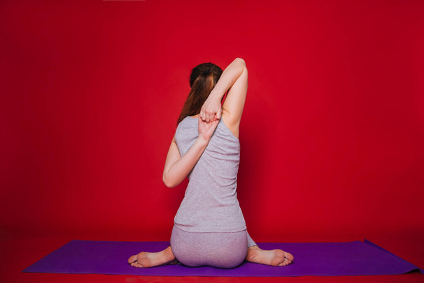 Atletická jóga, krásná mladá dívka cvičící Eka Pada Garudasan. Žena v černém sportovním oblečení na jednoduchém červeném pozadí - Fotografie, Obrázek