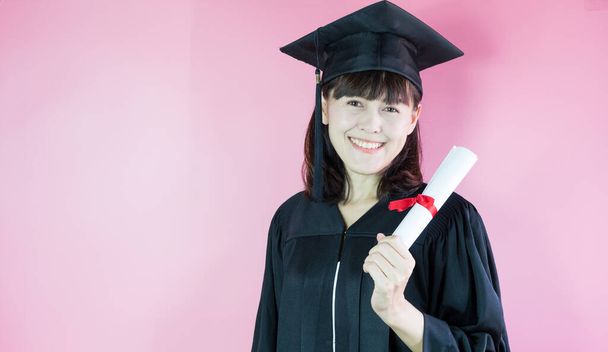 Felice laureata sorridente lei è in cappello di laurea e diploma in mano su sfondo rosa. - Foto, immagini