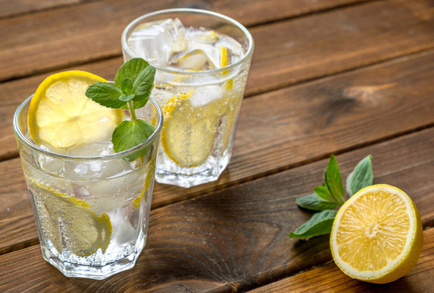 レモンドやモヒートのカクテルとレモン、ミント、アイスの入った2つのグラスが素朴な木製の背景にあります。 - 写真・画像