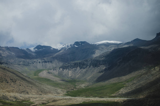 Stockfoto van een berglandschap. De lucht is bewolkt. Op de achtergrond ligt sneeuw op de top van de bergen. - Foto, afbeelding