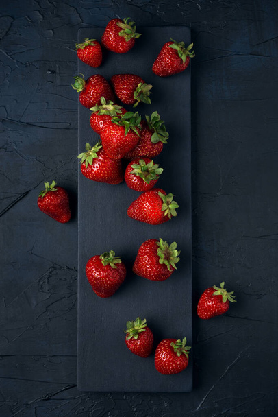 Reife rote Erdbeeren mit schwarzem Servierbrett auf dunkelblauem Hintergrund. Süßes Dessert aus frischen Beeren auf dem Tisch. Ansicht von oben. - Foto, Bild