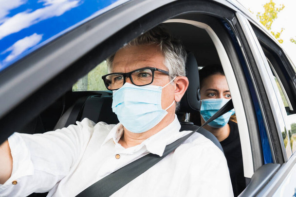 Új normális. Orvosi maszkos sofőr, aki egy utassal vezet autót. Egészségvédelem. Család az autóban, amit egy álarcos biztonsági és járványvédelmi koncepció véd. Coronavirus eszközök. Szociális távolság. - Fotó, kép
