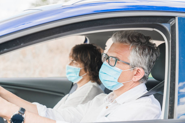 New normal. Driver with a medical face mask driving a car with a passenger. Health protection. Family in the car protected by a mask safety and pandemic concept. Coronavirus devices. Social distance. - Photo, image