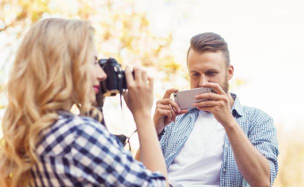 Muž a žena fotí s kamerou a smartphonem v podzimním parku. Láska, cestování a vztahy koncept. - Fotografie, Obrázek