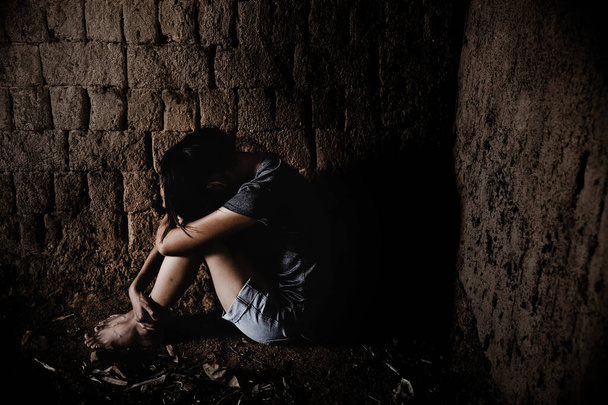Λυπημένη και απελπισμένη νεαρή Ασιάτισσα, η νεαρή γυναίκα νιώθει λυπημένη, η φτωχή κοπέλα κρατείται και κάθεται σε ένα βρώμικο πάτωμα.. - Φωτογραφία, εικόνα