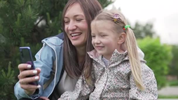 Äiti ja nuori tytär ottavat selfien matkapuhelimeen kävellessään puistossa kesällä. - Materiaali, video