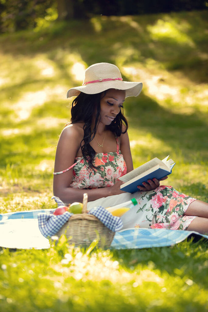 Attractive african woman is reading a book at picnic - Фото, изображение