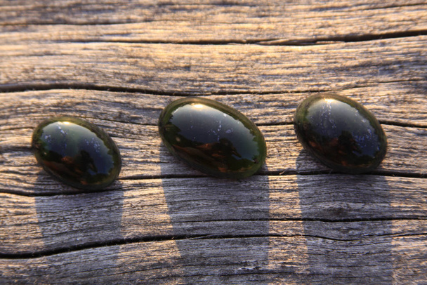 Pedra verde translúcida de jade preto na luz solar na madeira. O jade preto é verde escuro na cor, mas sob a luz é semi-transparente, apreciado por joalheiros porque a maneira como brilha
 - Foto, Imagem
