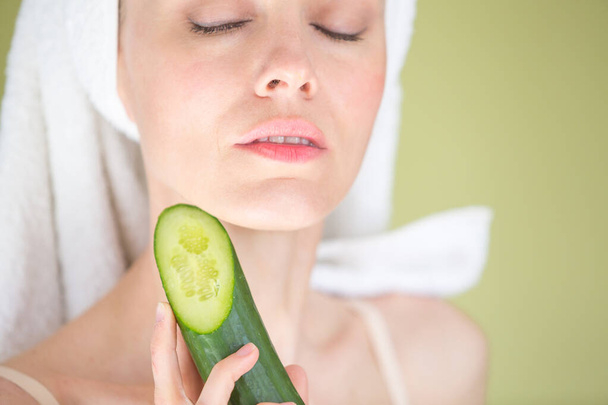  Beautiful young woman with facial mask on her face holding slices of fresh cucumber - Foto, afbeelding