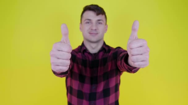 Man in pink plaid shirt smiles, raises hand and shows like on yellow background - Footage, Video