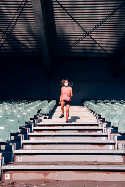 zdrowa, sprawna kobieta uprawiająca sport na stadionie - biegaczka na stadionie w masce ochronnej - Zdjęcie, obraz
