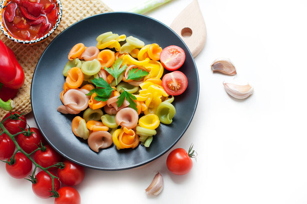Colorful pasta with tomatoes, garlic, parsley, pepper on a black plate. Pasta for child with tomato sauce on a white background. Top view - Photo, Image
