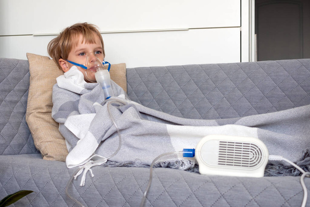 Little caucasian boy making inhalation with nebulizer at home. Child holds a mask vapor inhaler. Treatment of asthma. Concept of inhalation therapy apparatus. - Foto, afbeelding