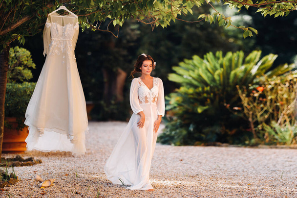 a beautiful bride stands next to a wedding dress with a boudoir attire next to a Villa in Italy.morning of the bride in Tuscany - Foto, Bild