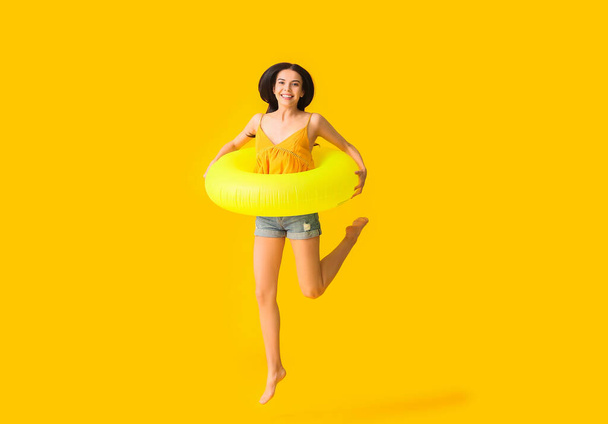 springende junge Frau mit aufblasbarem Ring auf farbigem Hintergrund - Foto, Bild
